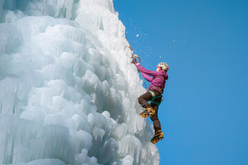 Alpinist woman with ice climbing equipment on a frozen waterfall