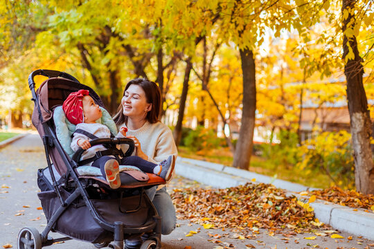 Mother showing yellow leaves to baby in baby stroller