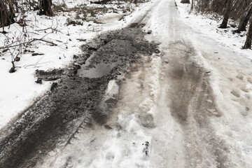 Wet dirty rural road with snow and puddles