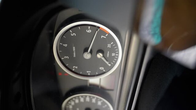 Black dashboard in car. Tachometer and speedometer circle. Numbers are illuminated on electronic panel. Tachometer needle moves and shows engine speed. Red mark shows over-revving. Vertical video. 