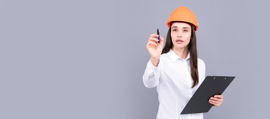 Serious woman in protective helmet with clipboard isolated on grey background. Young woman construction manager. Woman isolated face portrait, banner with mock up copy space.