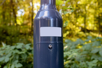Close up of a blank white sticker on metallic light post with forest in the background