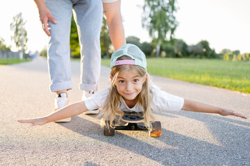  father pushing daughter lying on skateboard at park. Father and child girl have fun together. - Powered by Adobe