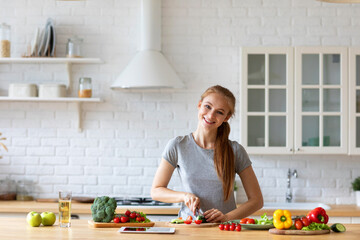 Young funny woman preparing vegetable salad in kitchen at home.