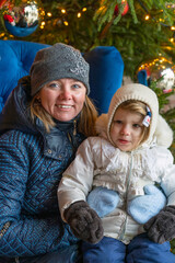 Obraz premium Happy Mother Holding Cute Baby Girl in Warm Clothes Against Christmas Tree Outdoors