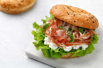 Sandwich with prosciutto, cream cheese and microgreens, bagel with ham, lettuce for breakfast on marble board. Space for text, close up.