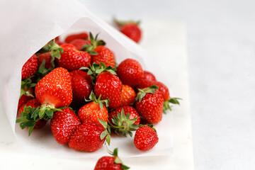 Delicious fresh strawberries in a paper bag on marble board, close up. Berry take away.