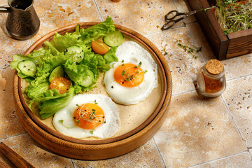 Breakfast with fried eggs, micro greens, and salad, cherry tomatoes. Beige ceramic plate, wooden tray