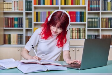 Teenage female student studying in library, using laptop