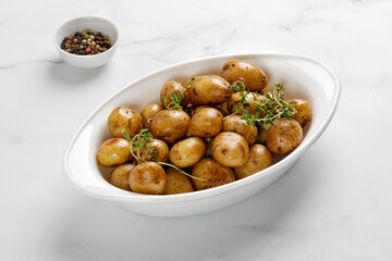 Roasted boiled young potatoes in white baked dish with thyme. Copy space.