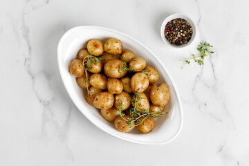 Young Fresh homemade boiled baby potatoes with thyme in baked dish. White marble background. Top view, copy space.