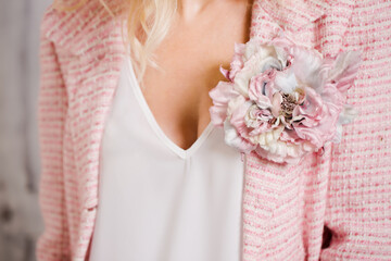 A pink tweed jacket with a brooch in the shape of a flower