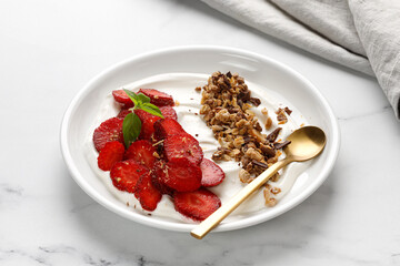 Fresh Organic Greek Yogurt with strawberries and granola in a white plate on marble background.