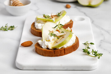 Bread toast with ricotta cheese, cream cheese, honey, pear, thyme on white board and marble table. Snack, bruschetta. Close up. - obrazy, fototapety, plakaty