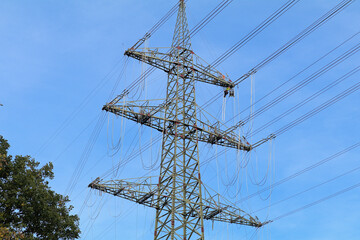 Workers on a high voltage pylon with high voltage lines in front of a blue sky