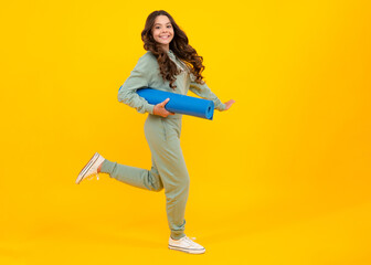 Fototapeta na wymiar Full length of a fitness teen girl in sportswear hold yoga mat posing over yellow background. Fitness model child wearing sport clothes. Run and jump. Girl in the sport concept.
