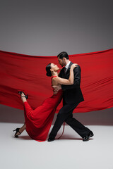 Side view of ballroom dancers performing tango on grey background with red fabric