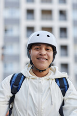 Vertical portrait of smiling food delivery worker wearing helmet while riding electric scooter