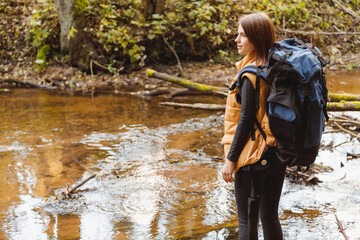 Woman with Backpack Crossing Forest River. Standing in Forest. Caucasian Female Camper in Hiking