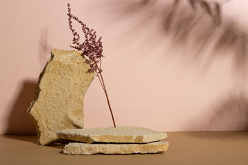 Background with an empty stack of stones and a dry flower on a beige background. Stone podium for cosmetic products. Pedestal for product presentation.