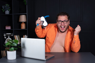 Funny fat man is sitting in the office and waiting for a vacation. Time to travel and swim in the sea. Office worker in an orange shirt with a mask and snorkel for swimming.