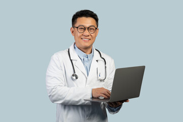 Social distance and new normal. Happy middle aged chinese man doctor in white coat and glasses with laptop