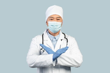 Calm mature japanese male doctor in white coat, protective gloves, mask showing crossed arms sign