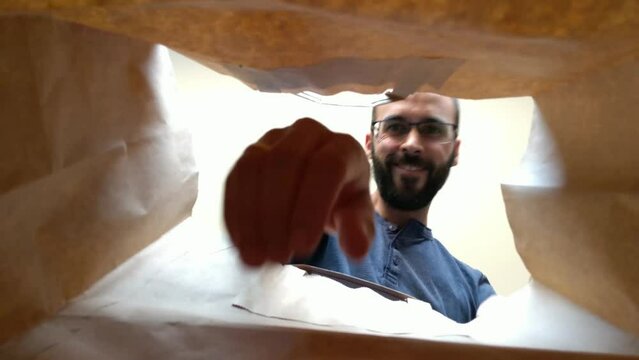 View from inside a paper bag of a bearded man and glasses taking out food