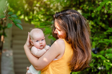 A young mother holds a baby in the park in the summer