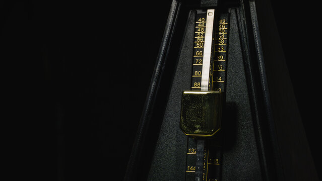 Mechanical metronome on a dark plain background: music, mechanical metronome, metronome, dark, black, background, isolated, gold, instrument, rhythm.