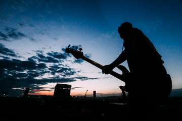 Silhouette of a guitar player on stage. Guitarist on a sunset background at the festival. 