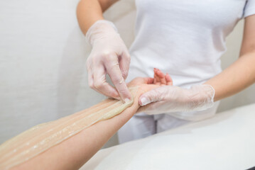 Obraz na płótnie Canvas Sugar paste hair removal procedure - shugaring. Cosmetologist applies sugar paste to the hand of a young woman.