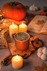 Cozy autumn still life: a cup of cappuccino, lights, a warm sweater, pumpkins, fallen leaves, a book and candles.The concept of wishing a cozy evening.Selective focus.Autumn background. Halloween card
