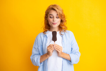 Young woman eats delicious ice cream, enjoys frozen dessert, dressed in casual clothes, isolated on yellow background.