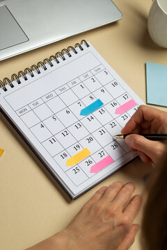 Hands of a woman planning and marking the dates of the schedule of business meetings on the calendar.