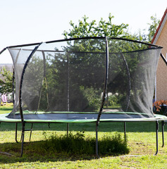 A trampoline for children is laid out in the yard in summer on a green lawn.