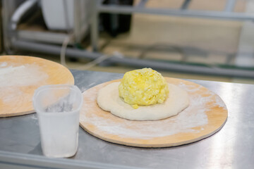Preparing ossetian pie with yellow filling - cottage cheese, cheese on kitchen table at cuisine of restaurant, bakery - close up. Professional cooking, pastry, gastronomy and food concept
