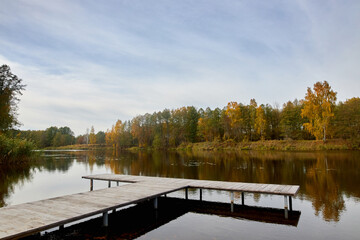 Wooden pier for mooring boats on the river bank near the autumn forest.