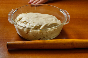 On a wooden table in a glass bowl there is a lush dough for baking.