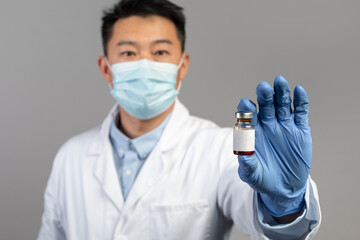 Serious mature chinese man doctor in white coat, protective gloves shows vaccine against covid-19 virus