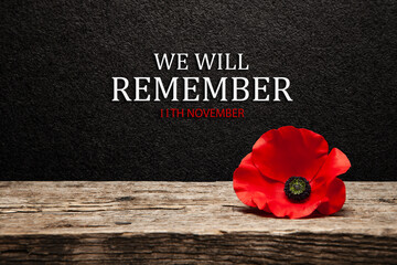 Poppy pin for Remembrance Day. Poppy flower on old beautiful high grain, detailed wood on black textured background with text.