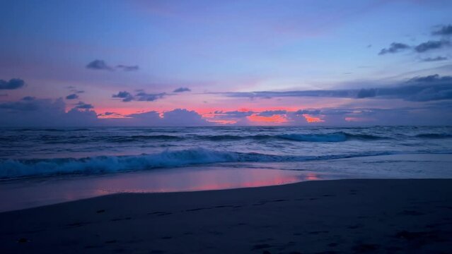 Amazing blue pink violet tropical sunset at ocean shore. Waves of sea rolling on beach at dark twilight. Last sun rays glow in the sky. Film grain texture. Soft focus. Live camera. Blur. Candid