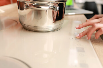 Female hand turns on electric hob closeup, finger presses sensor button on modern white induction...