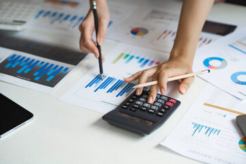 Working as a team with analytical graphs, business people are using calculators to calculate investment, turnover and profits displayed in a document on a desk at a conference room.