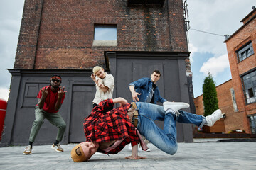 Motion shot of young man doing breakdance poses outdoors with all male dance team in background