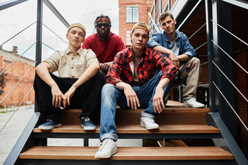Diverse group of boys wearing street fashion while posing on metal stairs in urban setting
