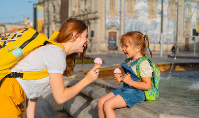 Happy young mother and little daughter sitting on the fountain with ice cream in the old European...