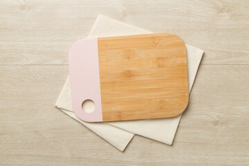 Cutting board with towel on wooden background, top view