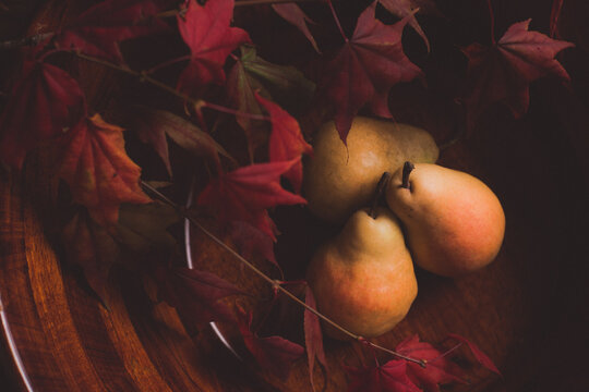 Colorful pears in a dark wooden bowl with fall leaves room for copy