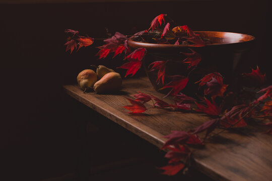 Yellow pears and brilliant red maple leaves in a wooden bowl on antique table top in moody light with copy space